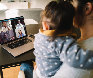 A mom holds her little one in front of a teleconferencing computer 