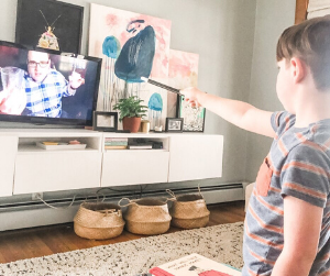 A boy points a magic wand at his television where The Great Scott is performing an illusion