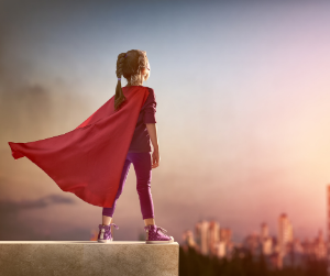 A girl in a super hero cape stands poised at the edge of the city she's about to save