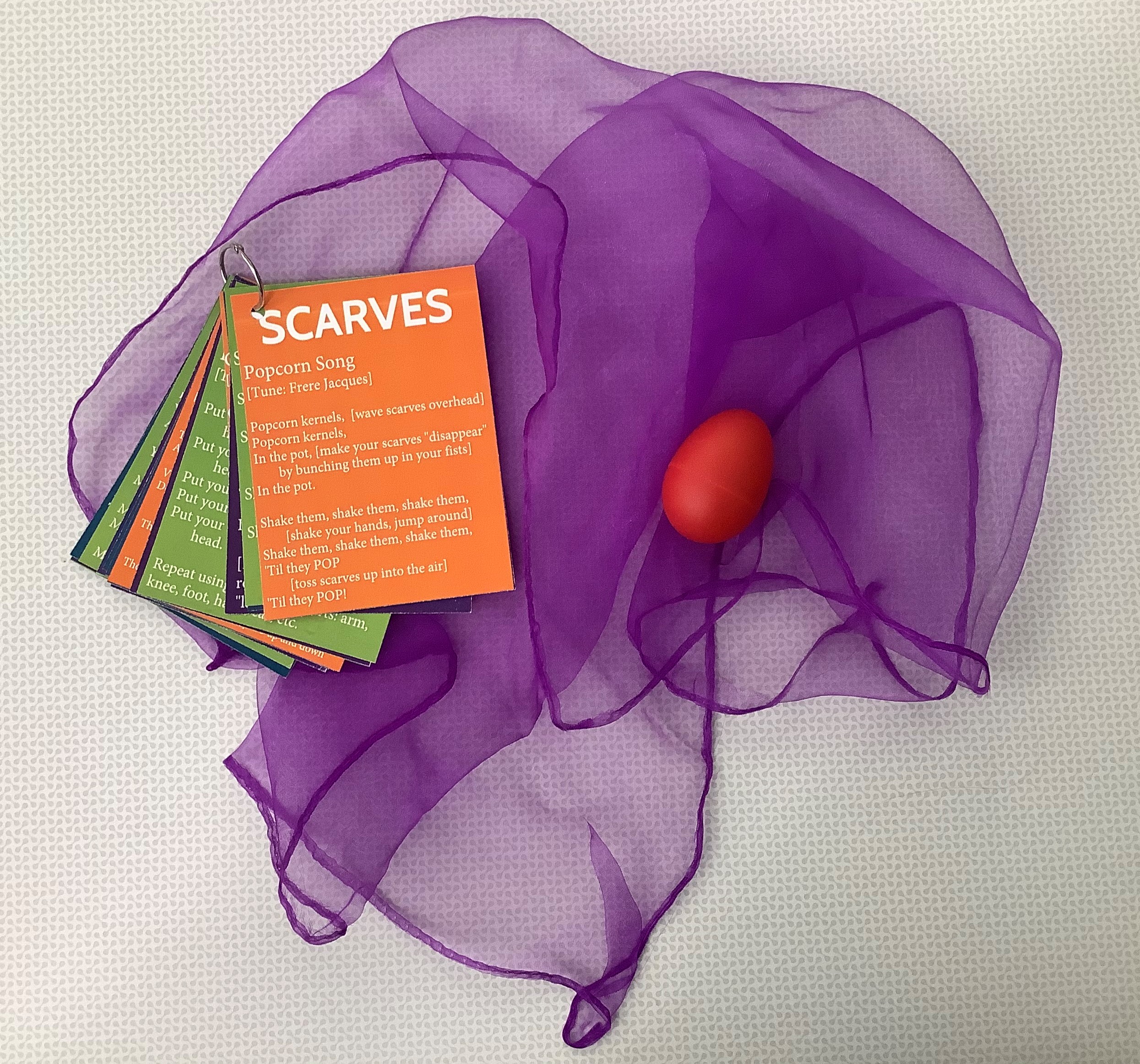 A purple scarf with a shaker egg and a booklet of activities