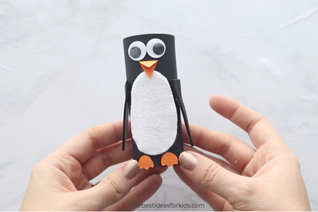 A penguin craft with googly eyes held by child's hands