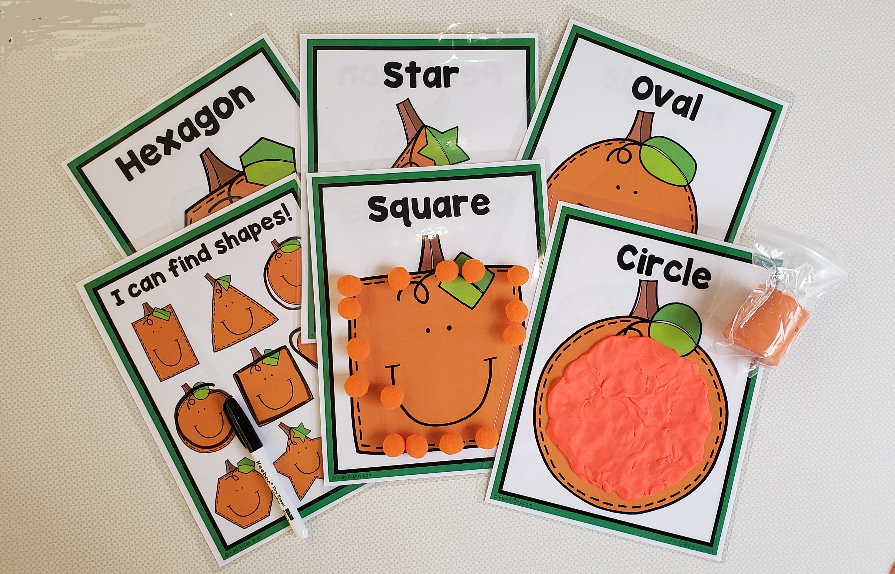 Image shows six laminated play mats with pumpkin shapes on them, a black dry erase marker, 15 pom-poms outlining a square-shaped pumpkin on one of the mats, orange play dough filling in a circle-shaped pumpkin on one of the other mats, and a bag of orange play dough.