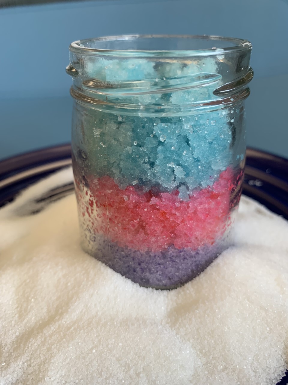 Jar of colorful sugar scrub standing in a bed of white sugar