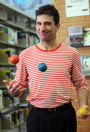 Chris Fascione in a red-and-white striped shirt, juggling a red ball and a blue ball.