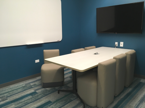 Study Room B interior shot with blue walls, whiteboard, mounted television, and rectangular table with six chairs
